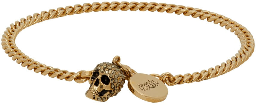 Curb chain bracelet in gold-tone brass. Swarovski crystal-embellished skull and logo disc at lobster clasp fastening.